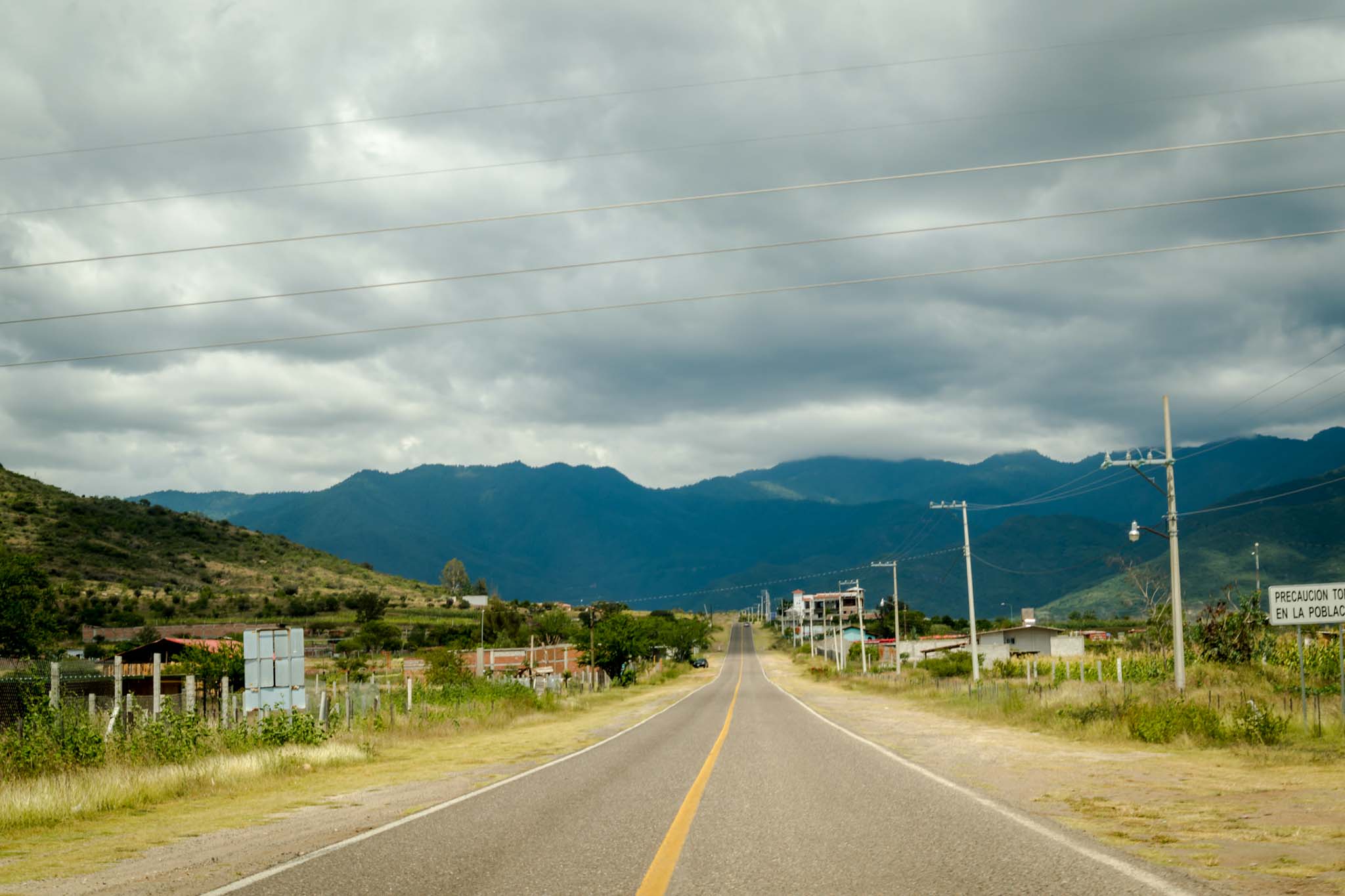 A road leading toward a small village in the Oaxaca countryside, mountains in the distance
